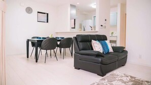 A modern living room with a black leather sofa, a dining table with chairs, and a kitchen area in the background. - youmeiyado kohama (Osaka)