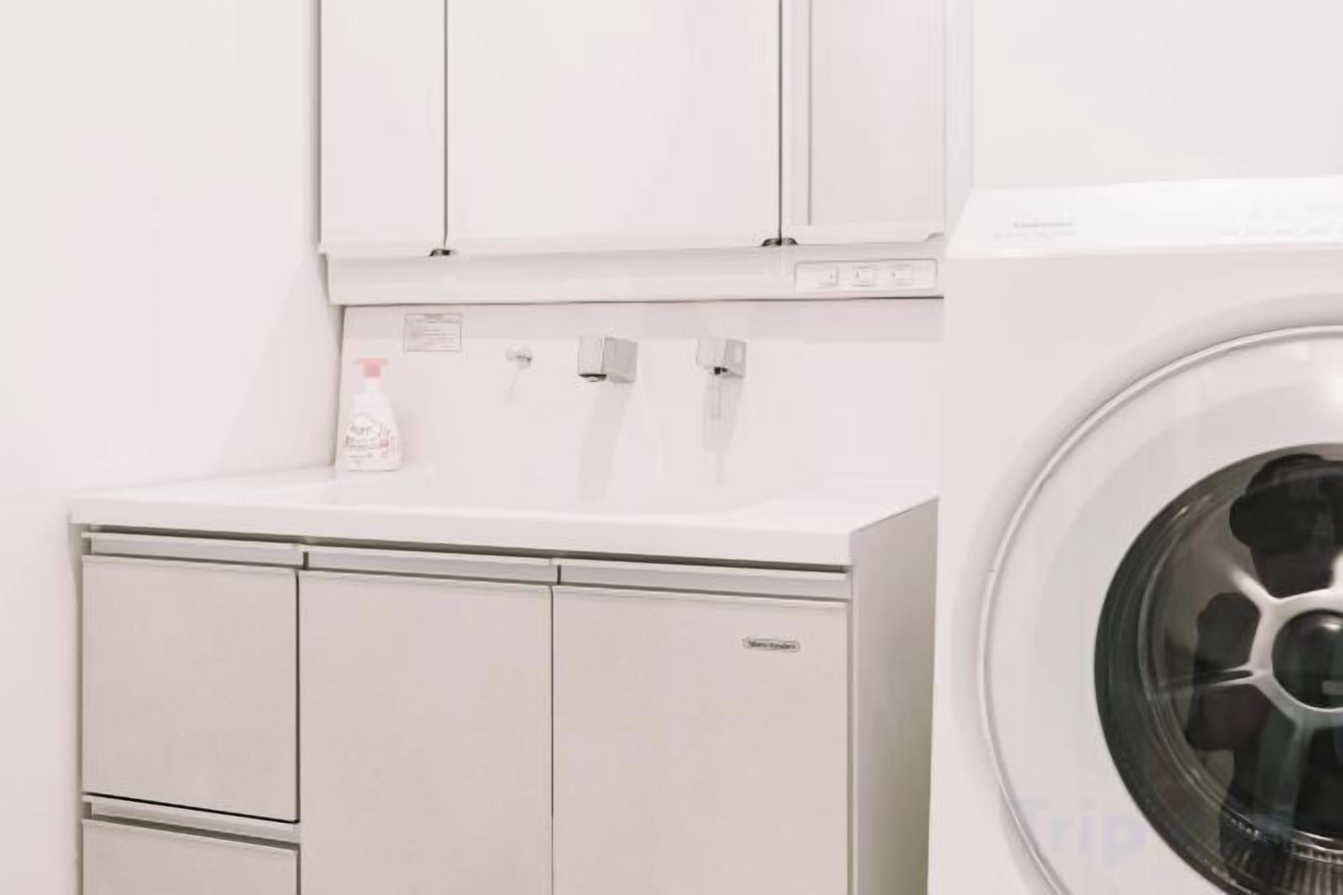 A white washing machine and a cabinet with a bottle of detergent.