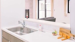 A modern kitchen with a double sink, a white countertop, and a wooden cutting board. - youmeiyado kohama (Osaka)