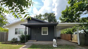 Una casa de un piso con fachada gris oscuro, un porche cubierto y un jardín delantero con una pequeña estatua.