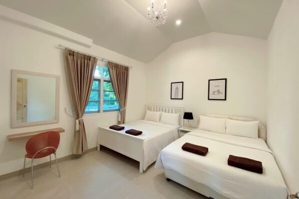 A hotel room with two beds, a red chair, a window with curtains, and framed pictures on the wall.