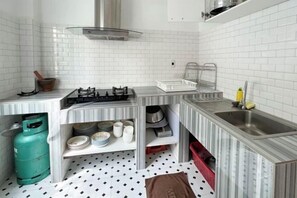 A compact kitchen with white tiled walls, a gas stove, a sink, and a gas cylinder.