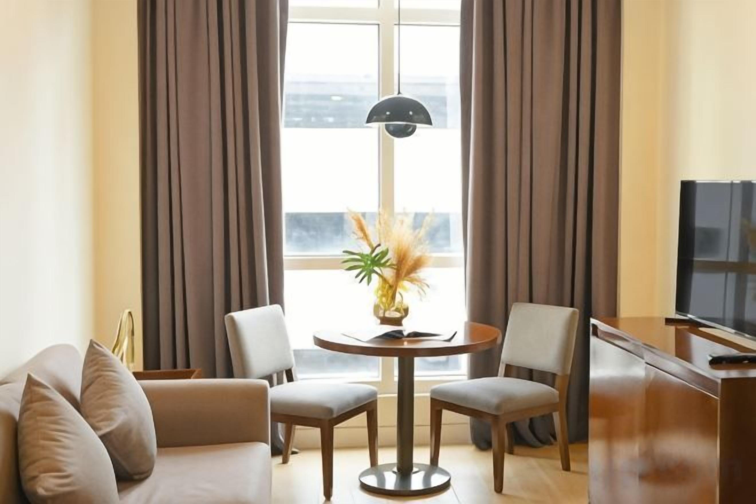 Une chambre d’hôtel avec un canapé, deux fauteuils, une petite table sur laquelle est posé un vase, et un téléviseur sur un meuble.