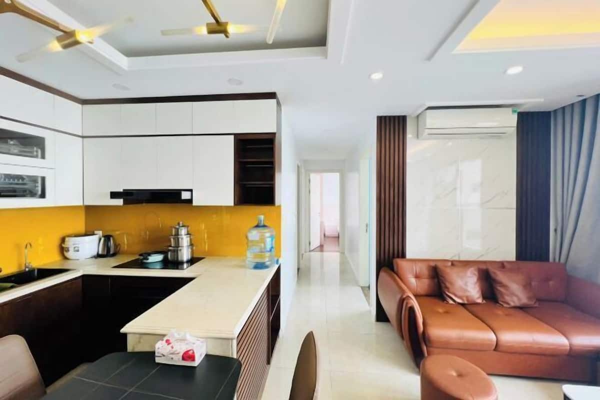 A modern hotel room with a kitchen area, a brown leather sofa, and a large window.