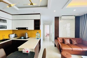 A modern living room with a brown leather sofa, a kitchen area with white cabinets, and a dining table. - Alex'housing Vinhome D'capitale luxury apartment (Hanoi)