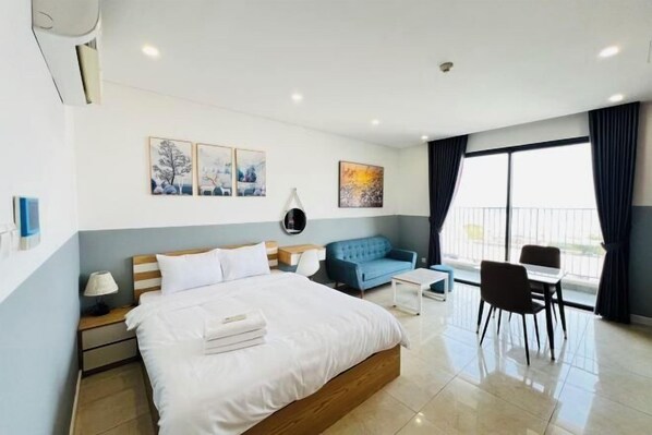 A modern hotel room with a large bed, a blue sofa, a small table, and a balcony with curtains. - Alex'housing Vinhome D'capitale luxury apartment (Hanoi)