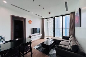 A modern living room with a flat-screen TV, a sofa, a coffee table, and a dining table. - Alex'housing Vinhome D'capitale luxury apartment (Hanoi)