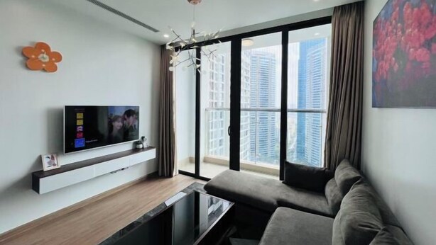A modern living room with a flat-screen TV, a sofa, and a large window with a city view. - Alex'housing Vinhome D'capitale luxury apartment (Hanoi)