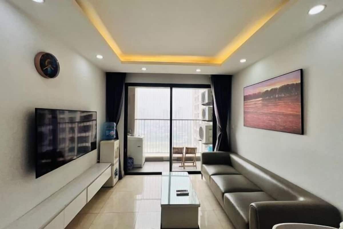 A modern living room with a flat-screen TV, a glass coffee table, a sofa, and a large window with a view.