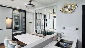 A modern kitchen with a marble countertop, bar stools, a built-in sink, and a decorative wall clock. - Alex'housing Vinhome D'capitale luxury apartment (Hanoi)