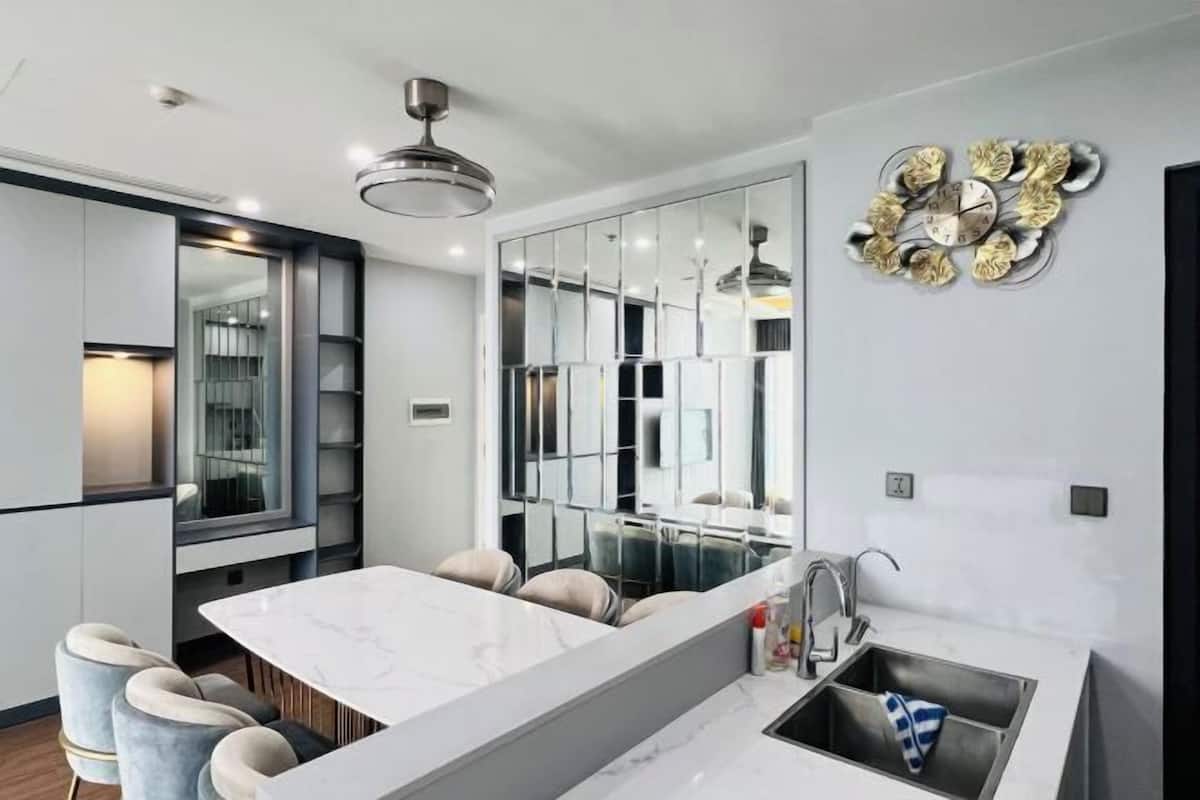 A modern kitchen with a marble countertop, bar stools, a built-in sink, and a decorative wall clock.