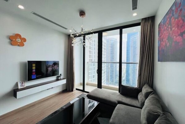 A modern living room with a large window, a flat-screen TV, and a sofa. - Alex'housing Vinhome D'capitale luxury apartment (Hanoi)