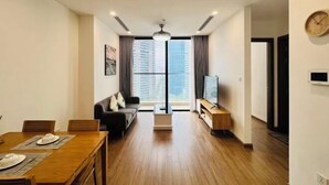 A modern living room with a dining area, a sofa, a TV, and a large window with curtains. - Alex'housing Vinhome D'capitale luxury apartment (Hanoi)