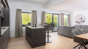 A modern kitchen with a central island, a dining area with a wooden table, and a grey sofa. - Bergresort Berwanger Hof by ALPS RESORTS (Berwang)
