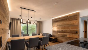 A modern kitchen with a wooden accent wall, a granite countertop, and a dining area with a wooden table and chairs. - Bergresort Berwanger Hof by ALPS RESORTS (Berwang)