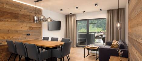 Un intérieur moderne avec un mur en bois, un coin repas comprenant une table et des chaises, un canapé et une grande fenêtre donnant sur un paysage verdoyant.
