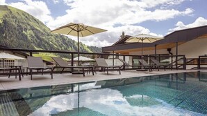 A pool area with lounge chairs and umbrellas, surrounded by mountains. - Bergresort Berwanger Hof by ALPS RESORTS (Berwang)