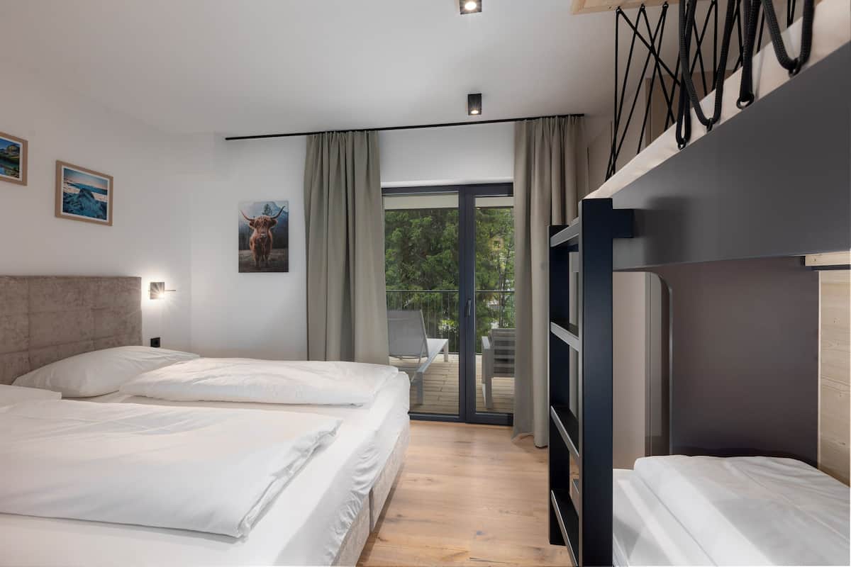 A modern hotel room with a large bed, a balcony with a view, and a wooden floor.