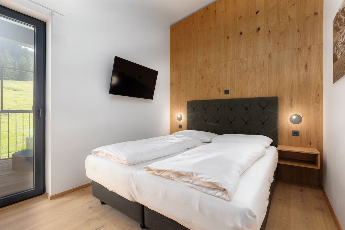 A bedroom with a bed, a TV mounted on the wall, and a wooden headboard.