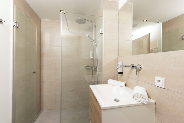 A modern bathroom with a glass-enclosed shower, a white sink, and a mirror above it.
