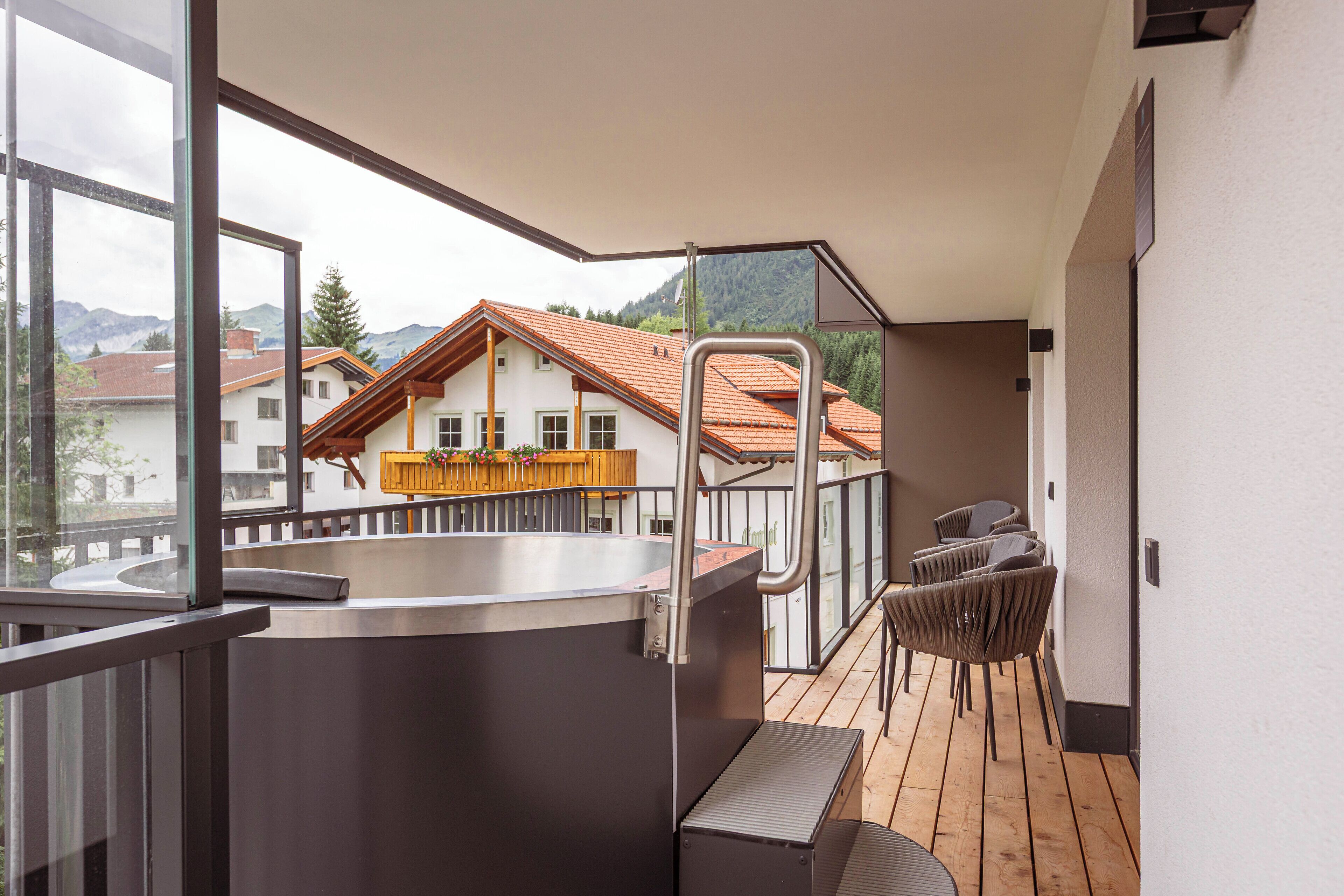 A balcony with a hot tub, wooden deck, and a view of a mountain and houses.