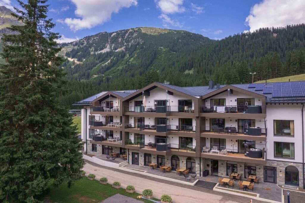 A multi-story hotel with balconies, outdoor seating, and a mountainous backdrop.