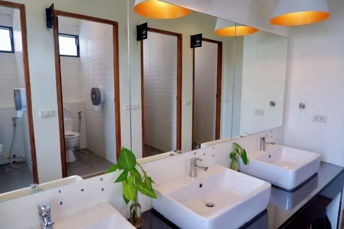 A bathroom with three sinks, a mirror, and a potted plant.