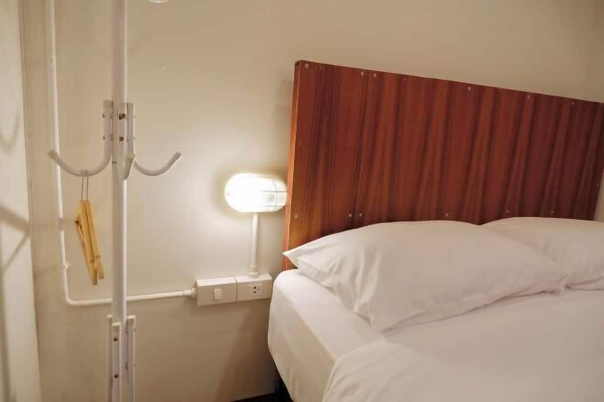 A hotel room with a wooden headboard, a bedside lamp, a white bed, and a wall-mounted hook.