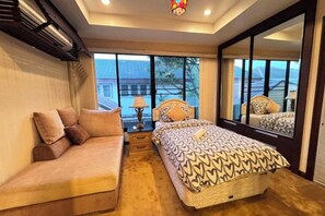 Une chambre avec un canapé, un lit recouvert d’une literie à motifs, une table de chevet, une lampe et un grand miroir qui reflète la pièce.