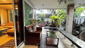 Een moderne woonkamer met een bank, een salontafel en uitzicht op een tuin met planten en een waterpartij.