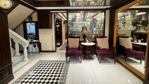 Un hall d’entrée spacieux avec un sol à carreaux, un escalier et un coin salon doté de fauteuils violets.