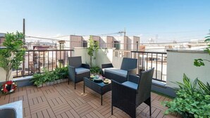Un balcon agrémenté de meubles en osier, de plantes en pot et offrant une vue sur le paysage urbain.