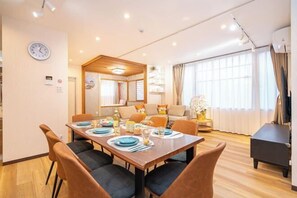 Un coin repas avec une table en bois dressée pour quatre personnes, une horloge au mur et un canapé à l’arrière-plan.