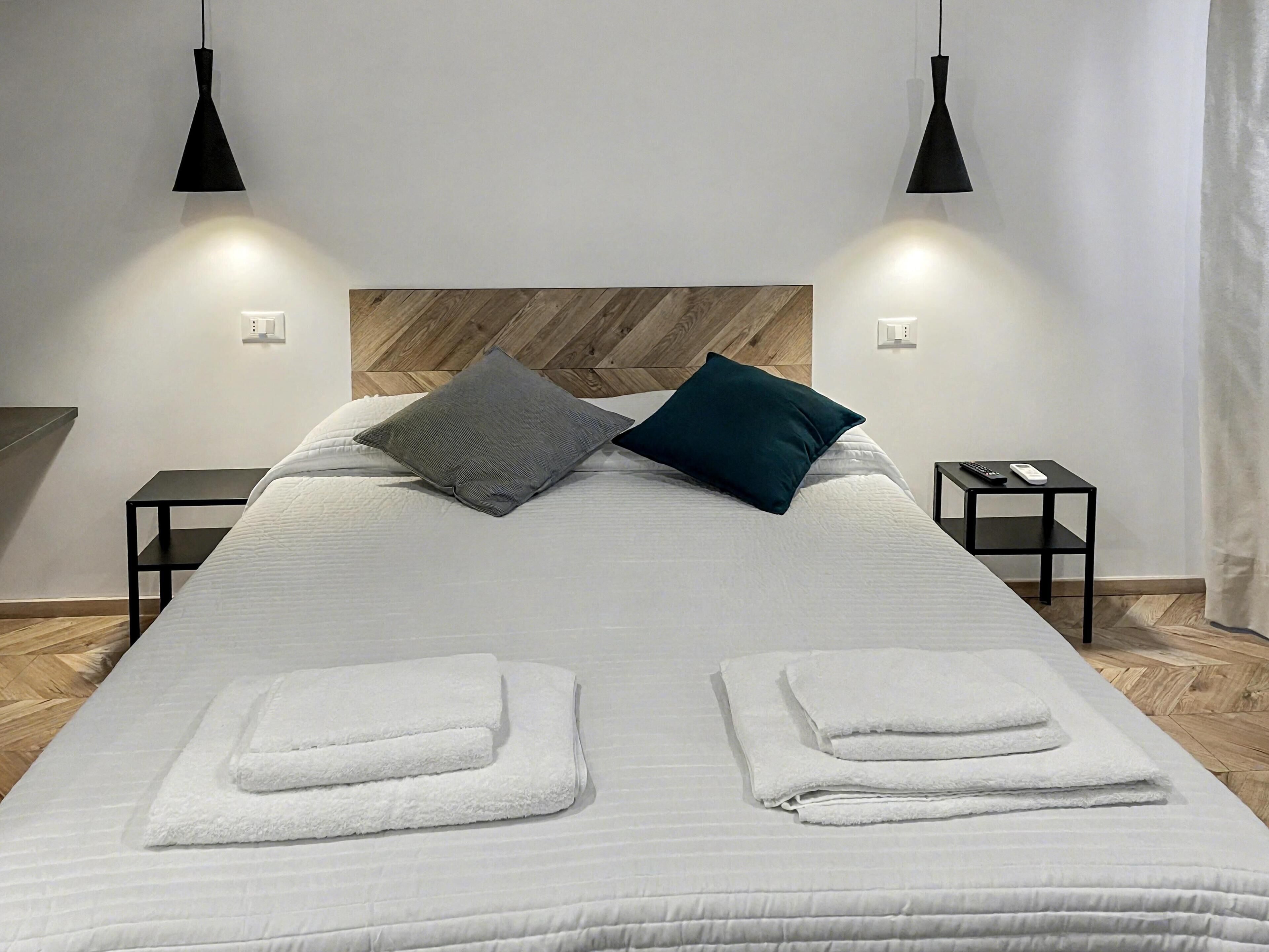 A neatly made bed with two pillows, a wooden headboard, and two bedside tables with remote controls.