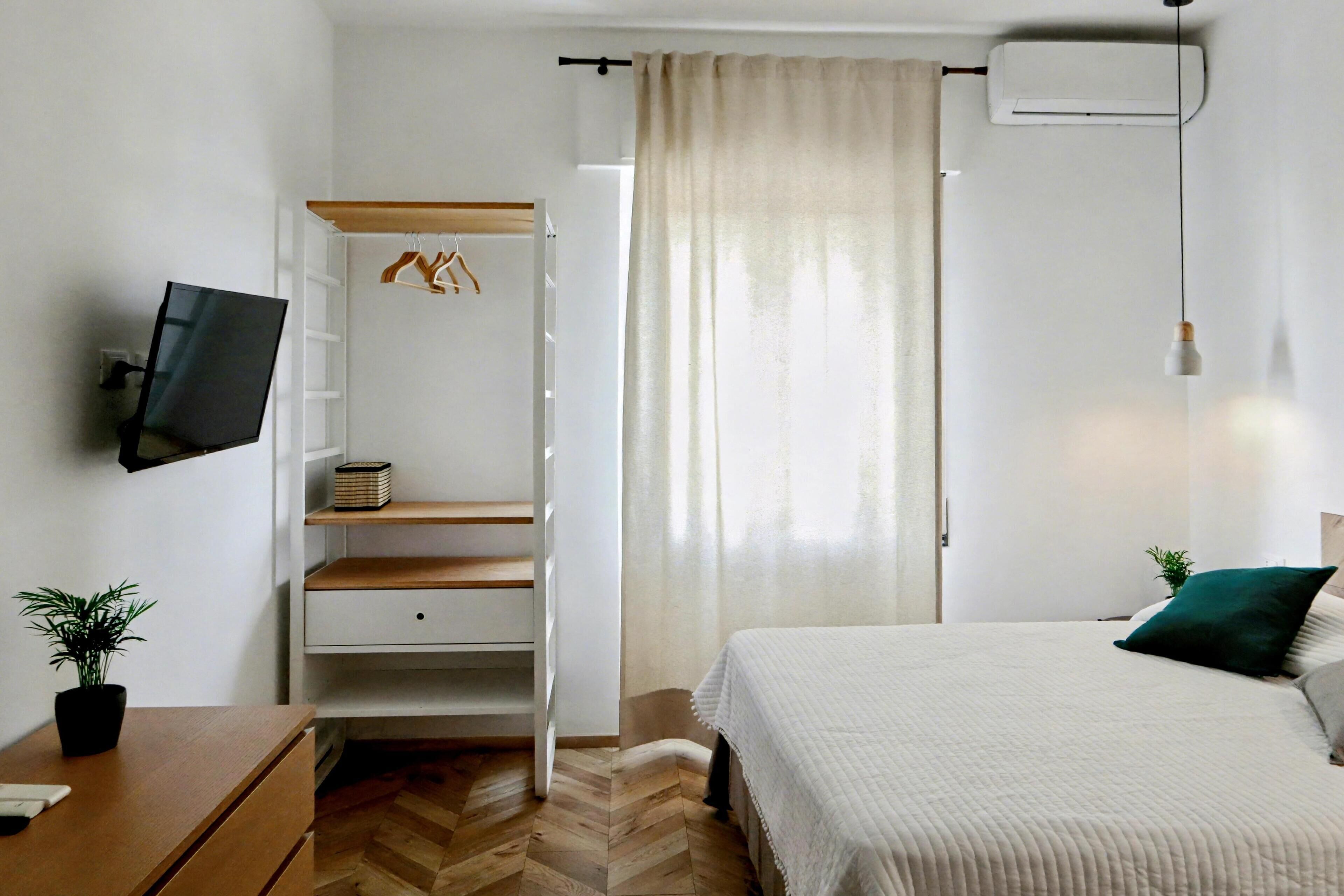 Quarto com cama, televisão na parede, guarda-roupa e janela com cortinas.