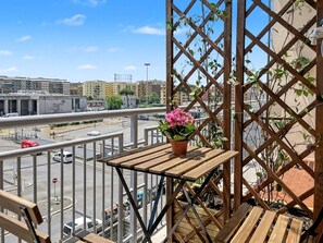A balcony with a wooden table and a potted plant, overlooking a city street with buildings and a highway. - Bed and Breakfast Casa Valentina (Rome)