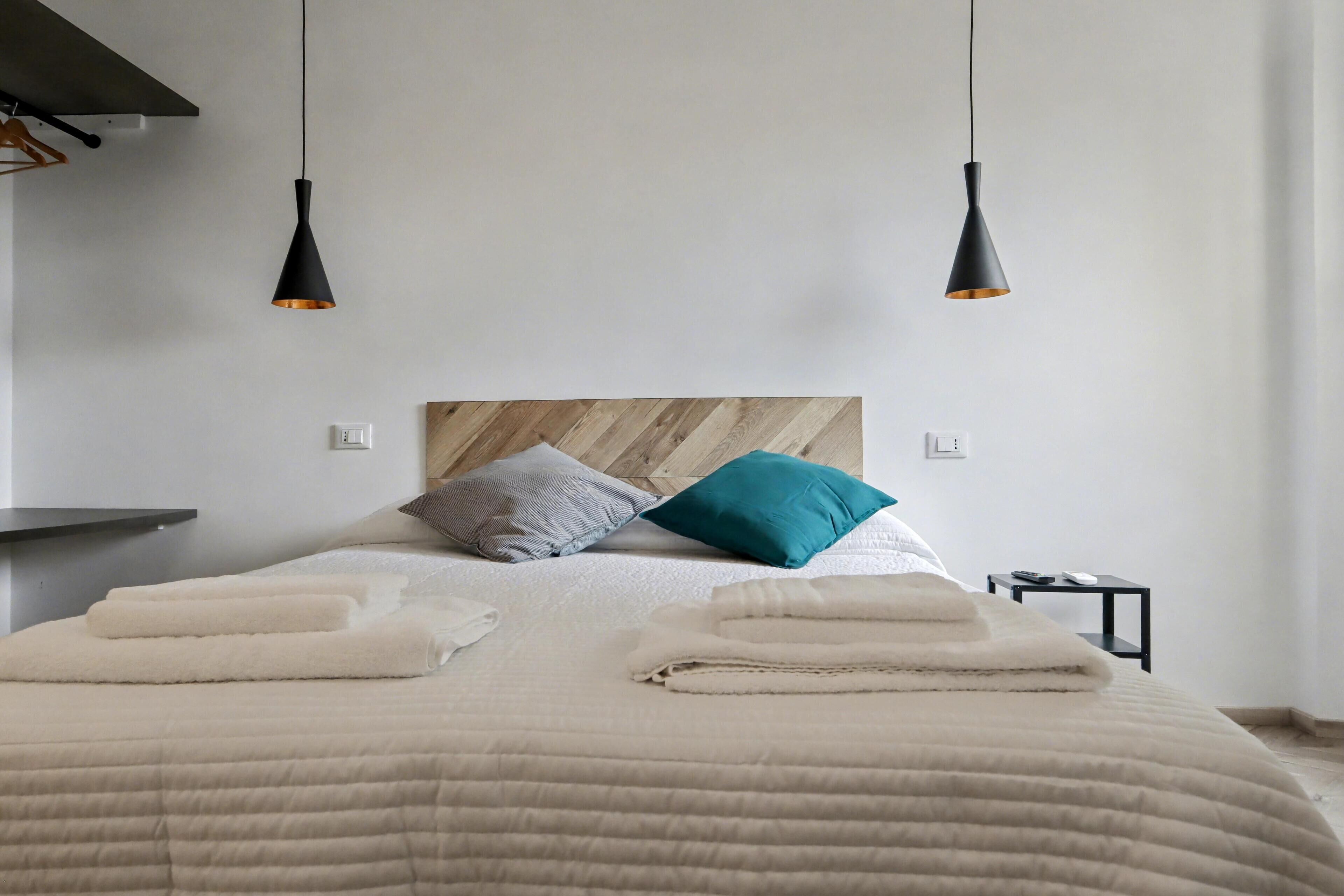 A neatly made bed with a wooden headboard, two bedside tables, and two pendant lights.