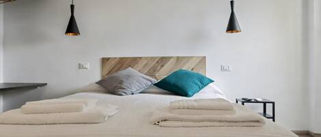 Una cama bien hecha con un cabecero de madera, dos mesitas de noche y dos lámparas colgantes.