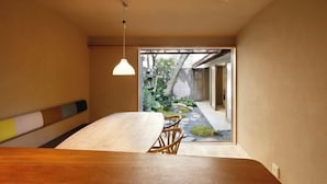 A minimalist room with a wooden table, two wicker chairs, a hanging light fixture, and a view of a garden through a glass door. - Kyo No Ondokoro Kamanza Nijo #2 (Kyoto)