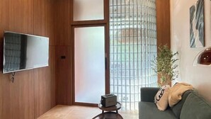 Un salon moderne avec un téléviseur à écran plat fixé au mur, un canapé vert et une petite table agrémentée d’un objet décoratif.