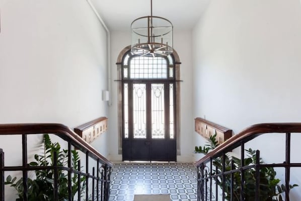 A staircase with a patterned floor leading to a door with a glass panel and a metal railing. - NOA - Lüleci Hendek 54 (Istanbul)
