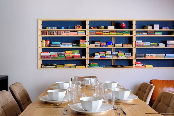 A dining area with a wooden table set for four, surrounded by chairs, and a bookshelf with books and decorative items.