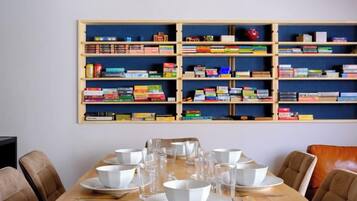 A dining area with a wooden table set for four, surrounded by chairs, and a bookshelf with books and decorative items.
