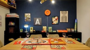 A dining area with a table set for four, surrounded by chairs, with a dark blue wall in the background featuring framed artwork and a large letter 'A'. - Board Game House Tokyo (Tokyo)