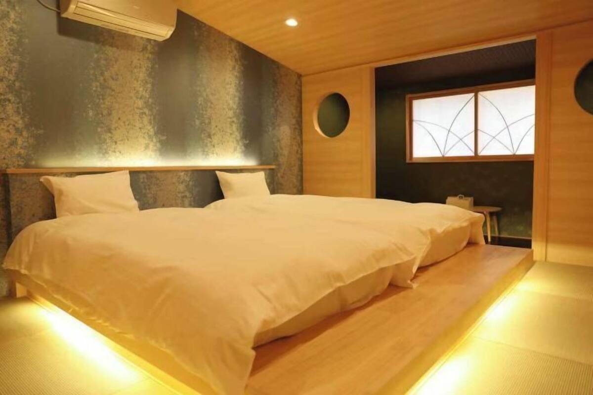 A room with a large bed, a small table, and a window with a geometric design.