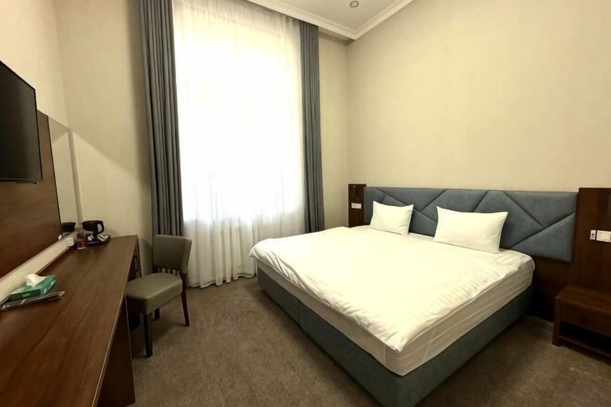 Ein Hotelzimmer mit Bett, Schreibtisch, Stuhl, Fernseher und einem Fenster mit Vorhängen.