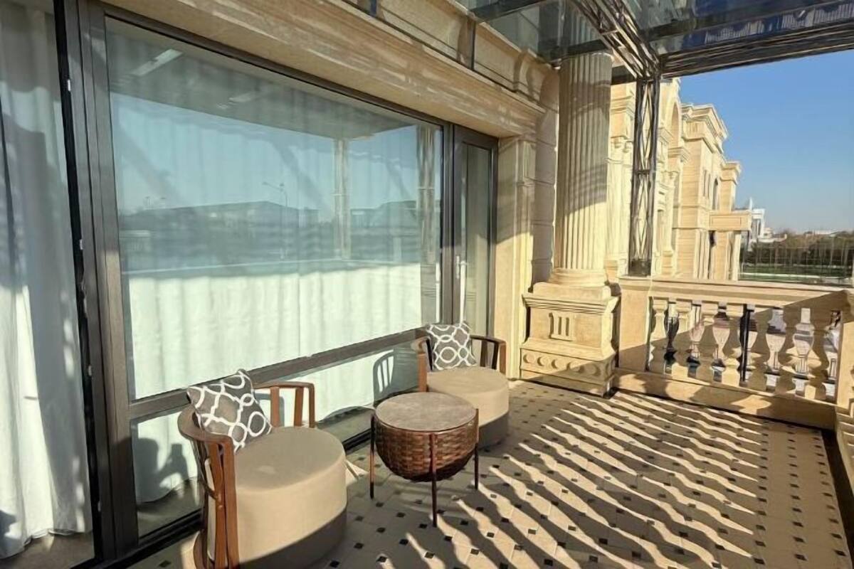 Ein Balkon mit Blick auf klassische Architektur, einer Glastür und einer Sitzecke mit rundem Tisch und Stühlen.