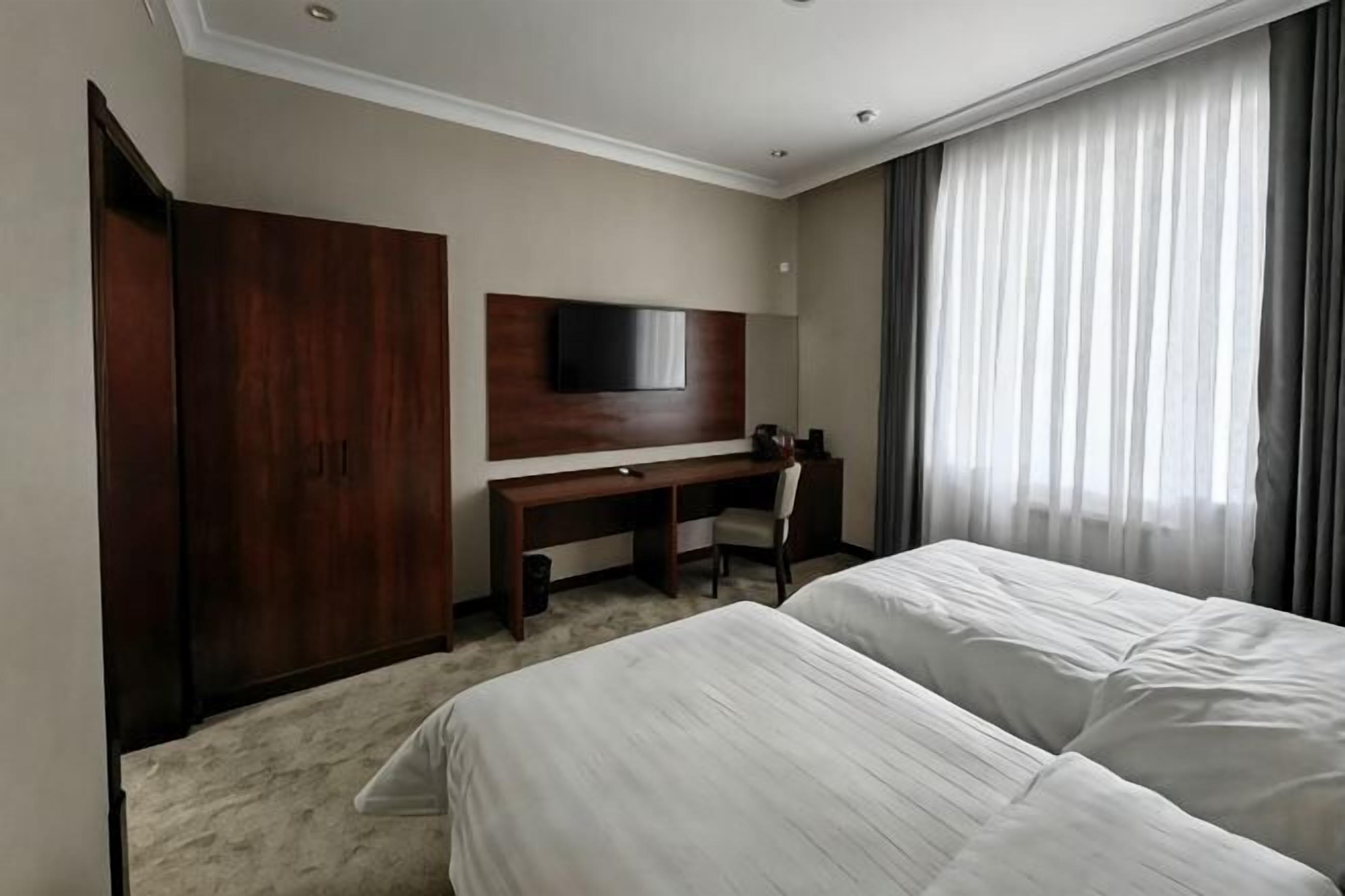 A hotel room with a bed, a desk, a chair, a TV, and a wardrobe.