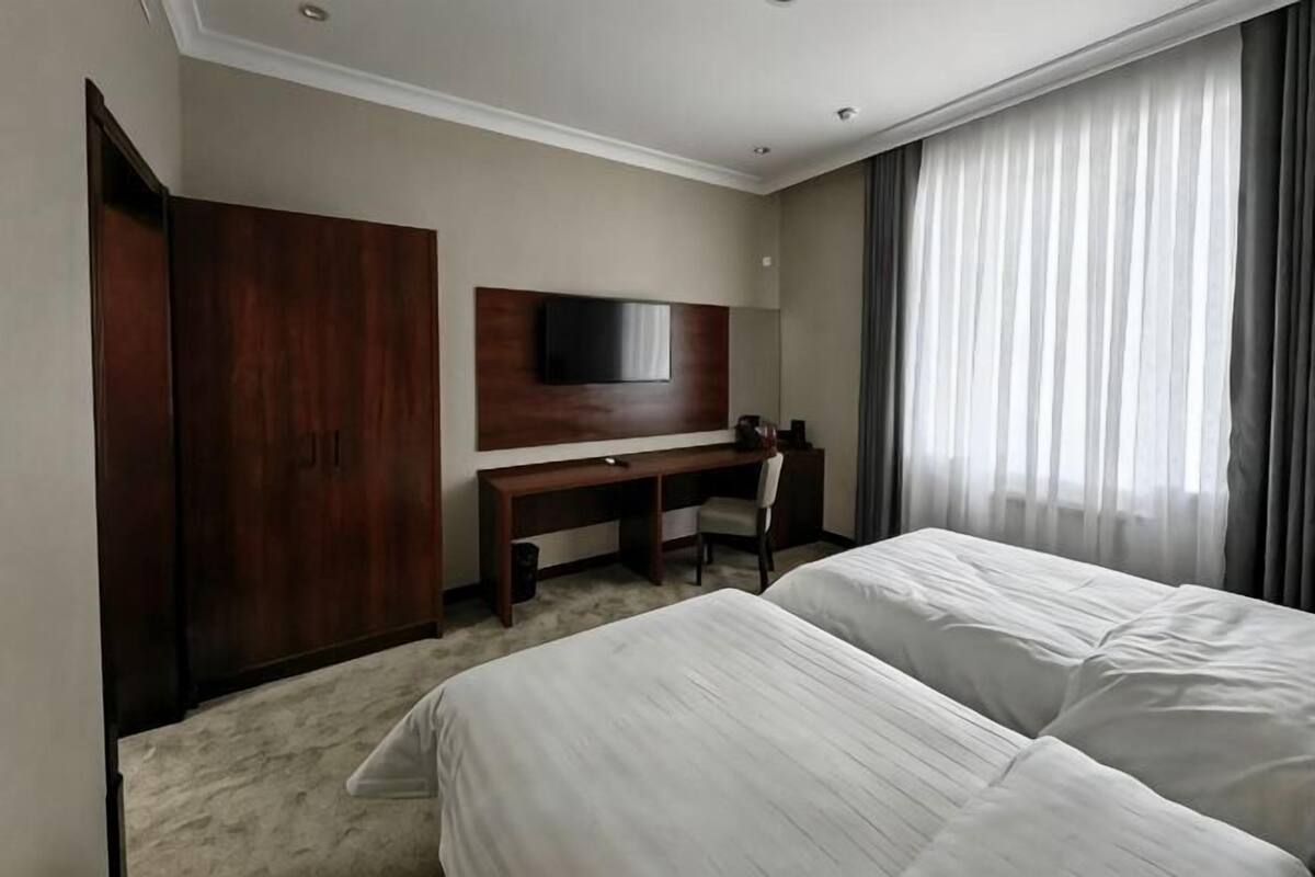 Ein Hotelzimmer mit Bett, Schreibtisch, Stuhl, Fernseher und Kleiderschrank.