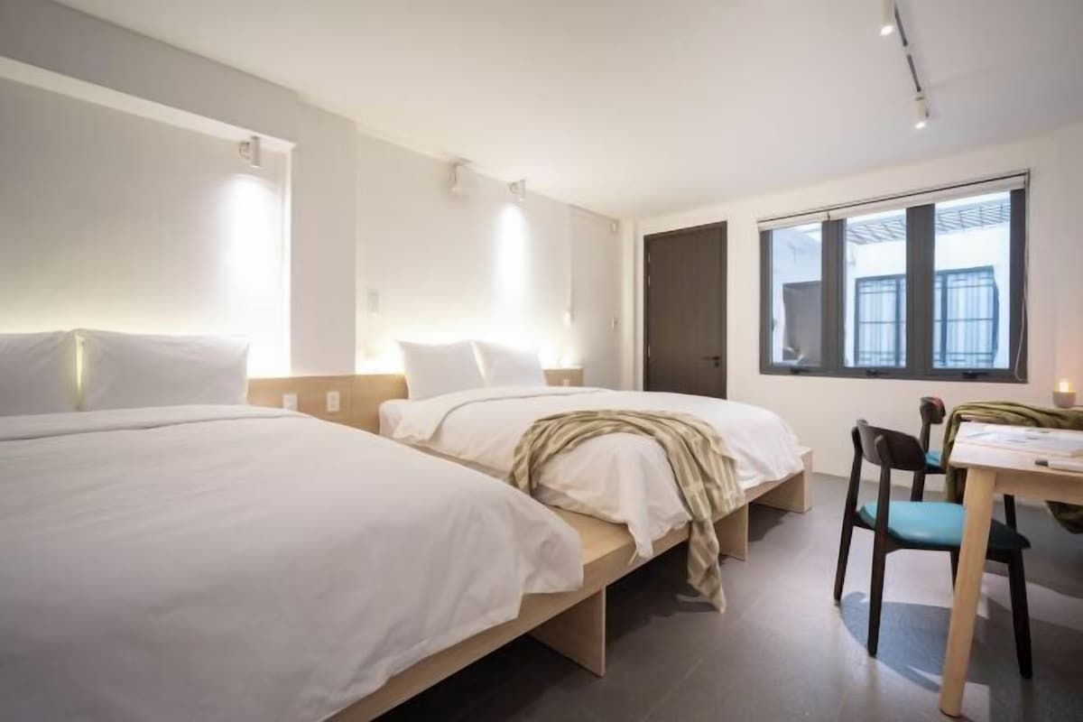 A modern hotel room with two beds, a desk, and a chair.
